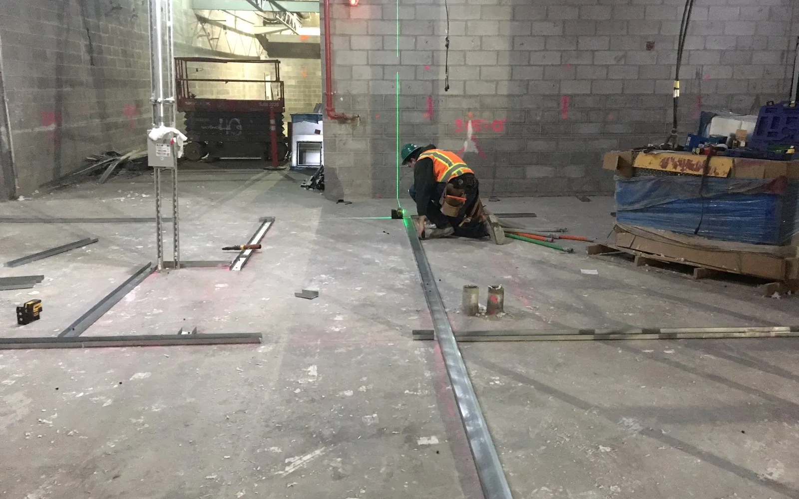 A fitter setting out partition tracks on the floor of a new office, following a green laser line